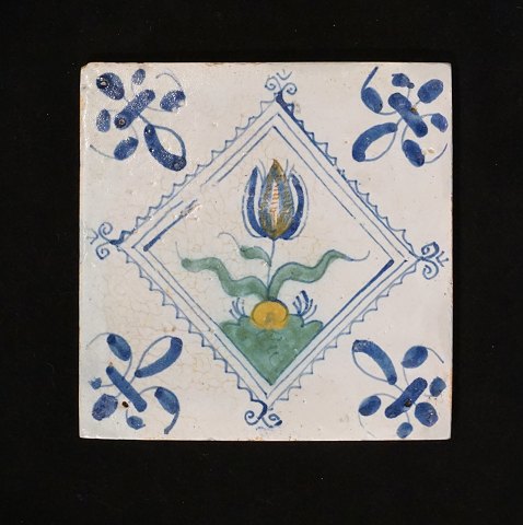 A 17th century polychrome decorated Dutch tile 
with a flower. Circa 1620-40. Size: 13x13cm
